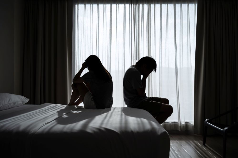 man and woman sitting back to back in a dark room in distress